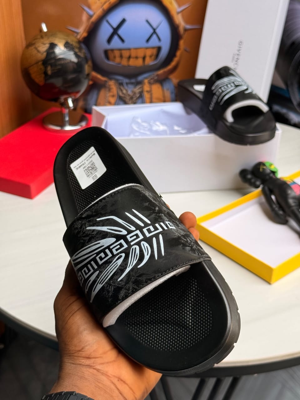 Hand holding black Versace slide with white pattern and text.