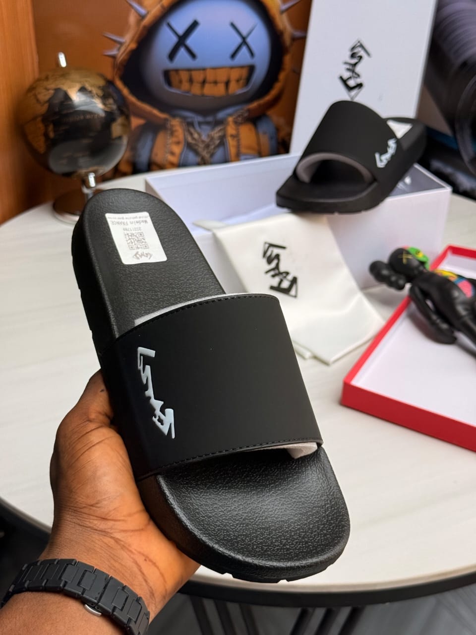 Hand holding black slide with white YSL logo on strap.