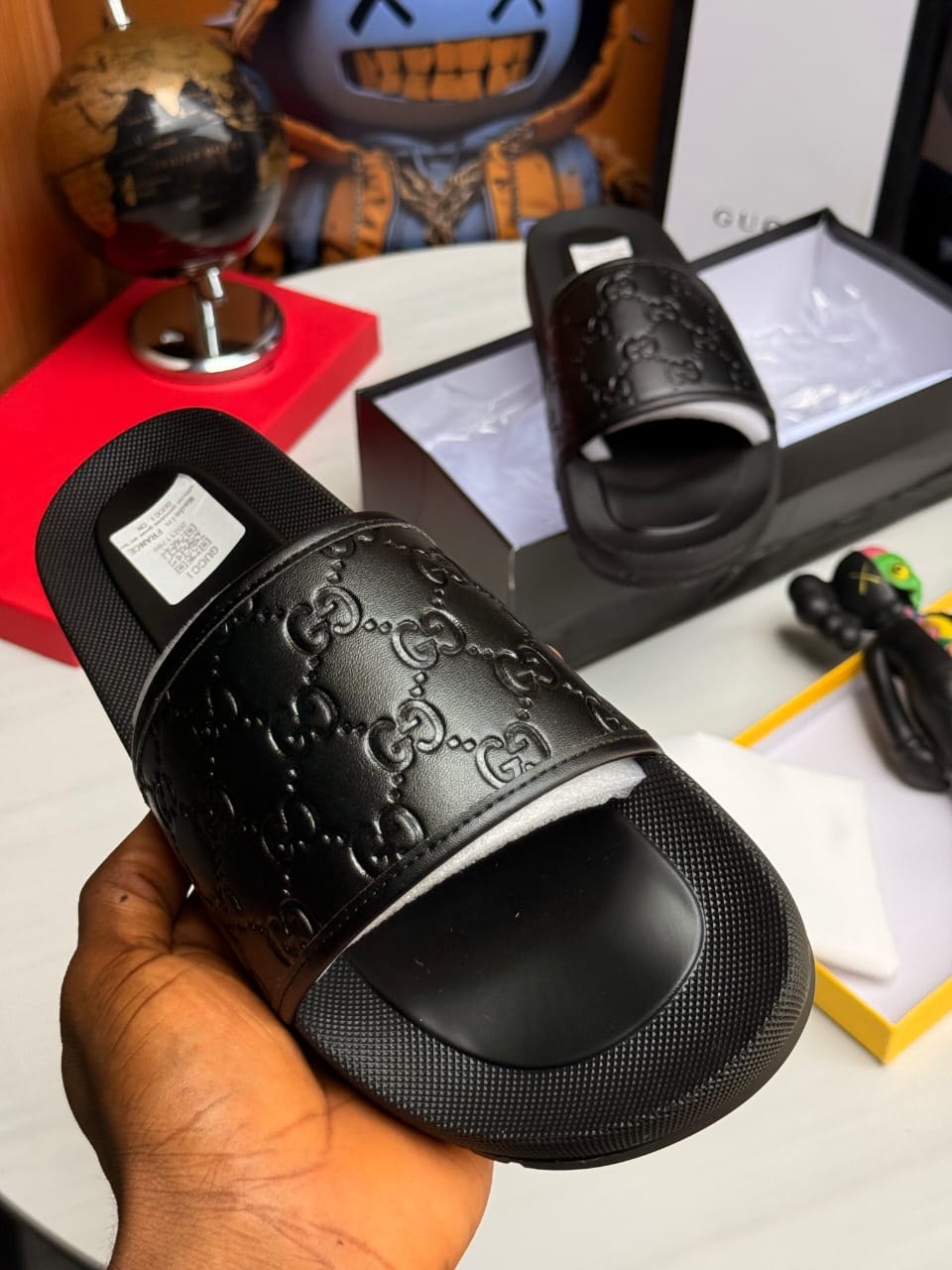 Hand holding black Gucci GG monogram slide with embossed pattern.