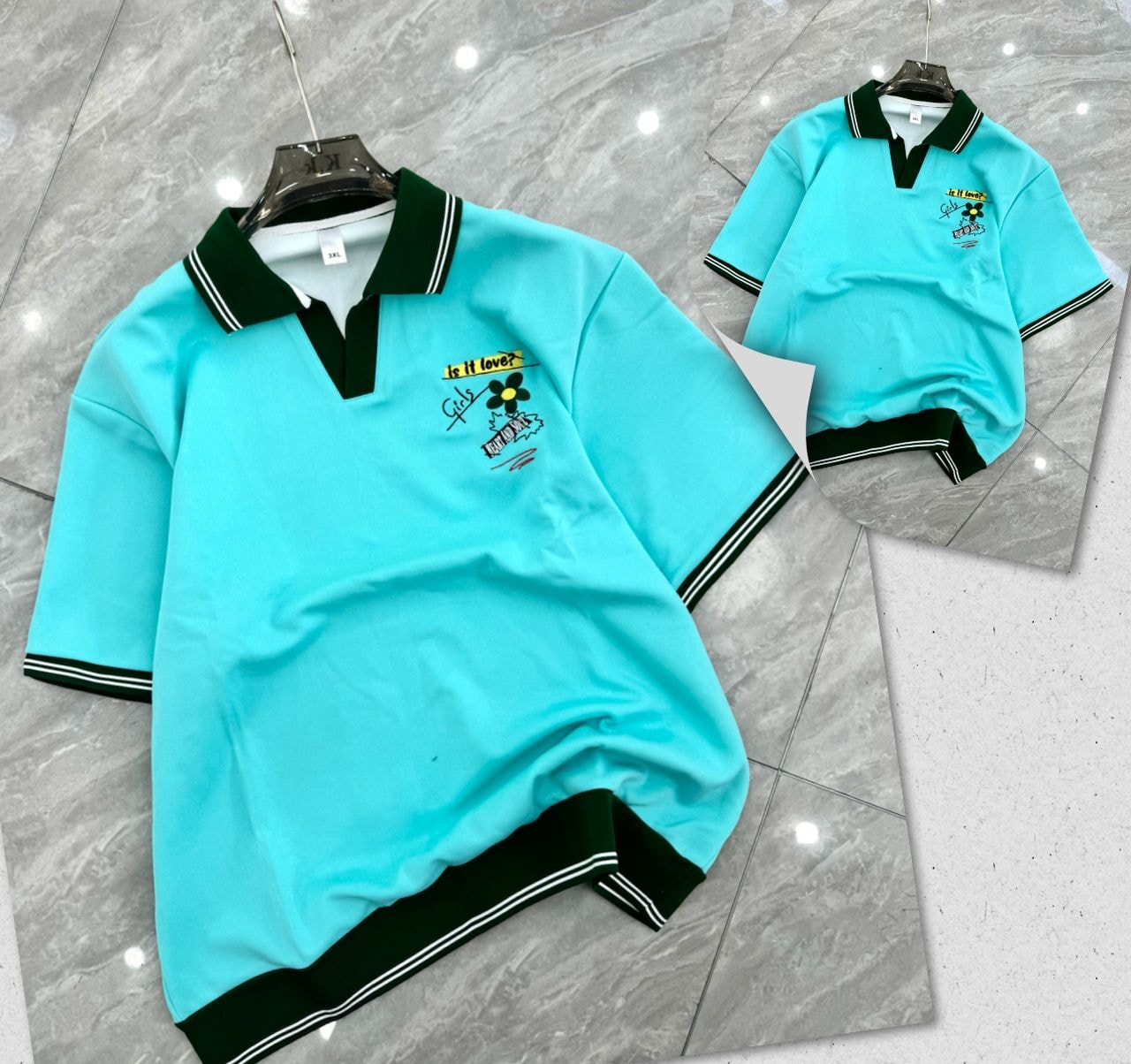Light blue polo shirt with green trim and chest embroidery on hanger and flat lay.