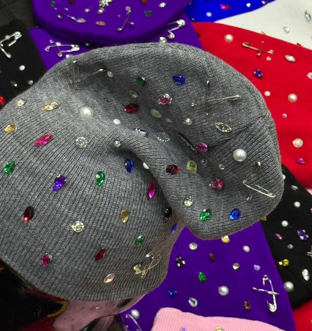 Close-up of gray rhinestone beanie showing detailed embellishments with gems, pearls and safety pins.