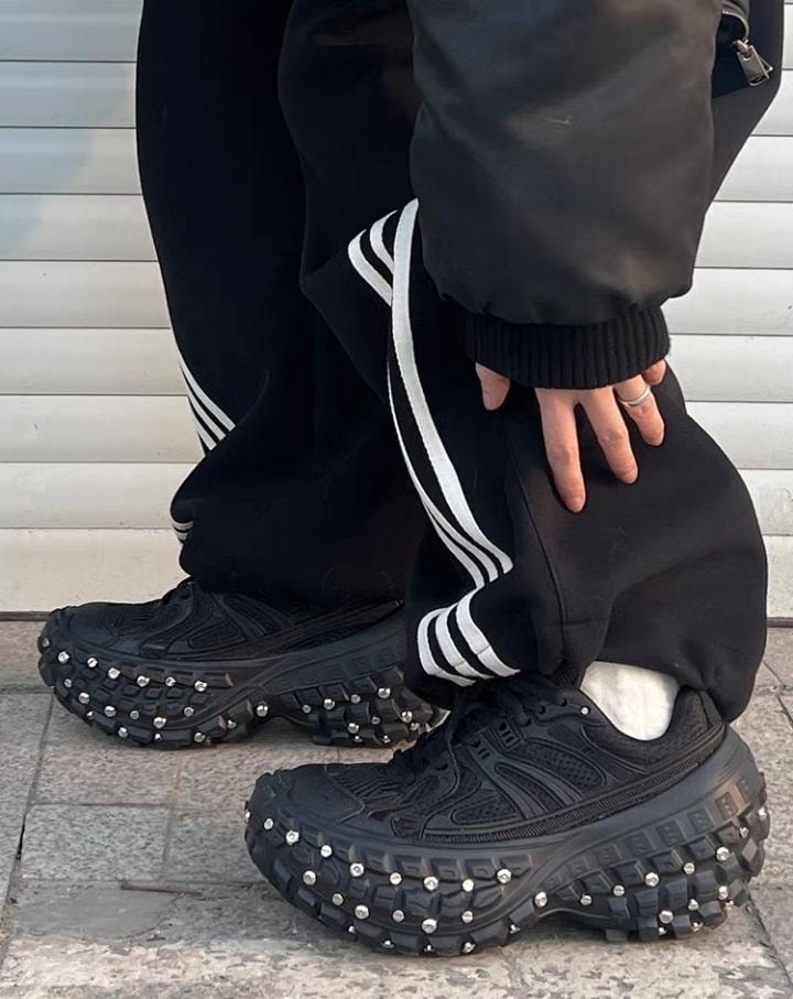 Person wearing black studded platform sneakers with black track pants.