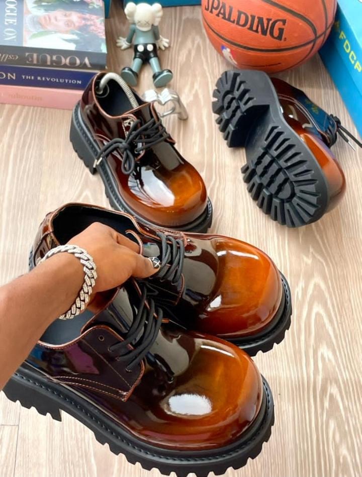 Brown patent leather platform derby shoes with chunky soles shown in lifestyle setting.
