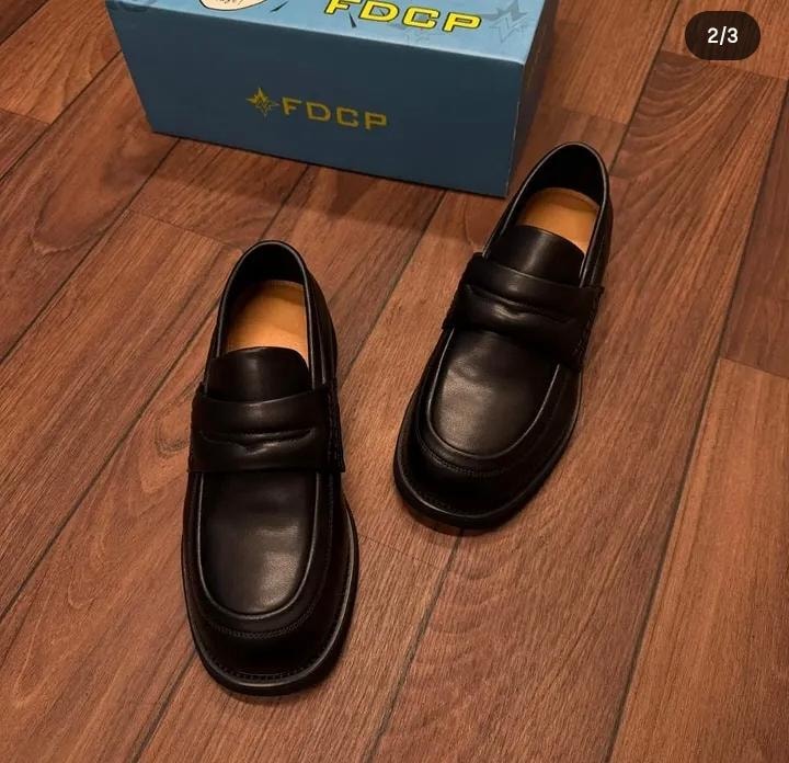 Black leather FDCP loafers on wooden floor with brand box.