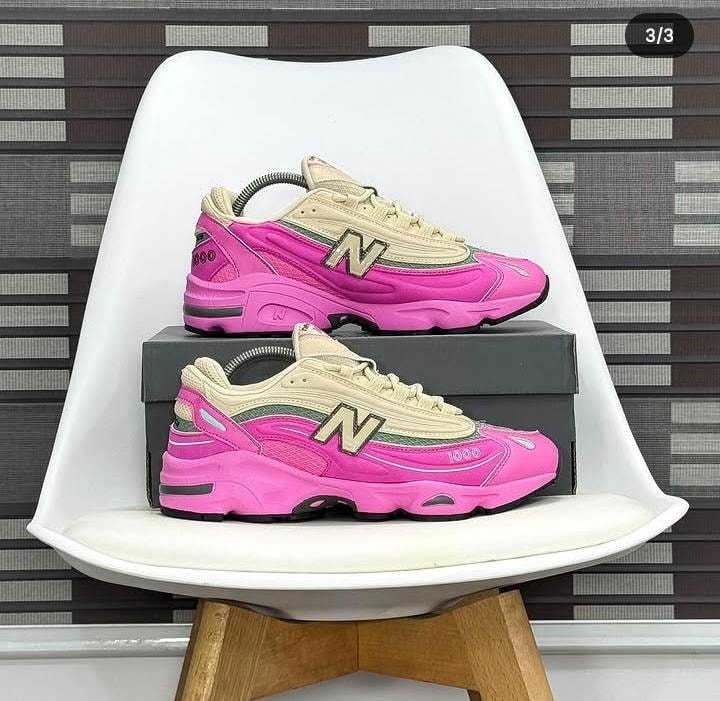 New Balance 1000 sneakers in pink with beige and green accents on white chair.