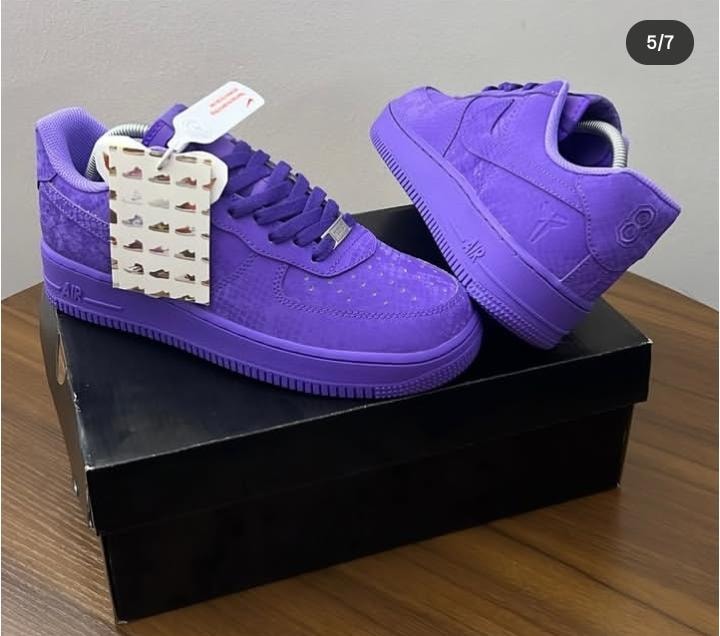 All-purple Nike Air Force 1 low sneakers displayed on a black box showing side and back angles with attached tag.