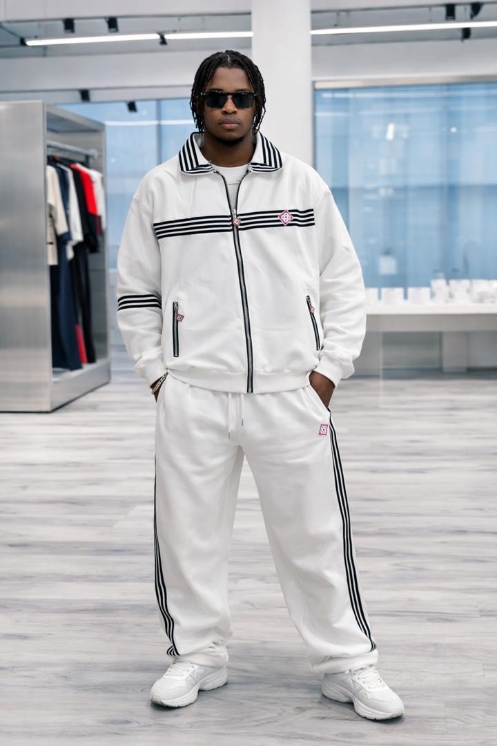 Man modeling white tracksuit set with black stripes and logo in studio setting.