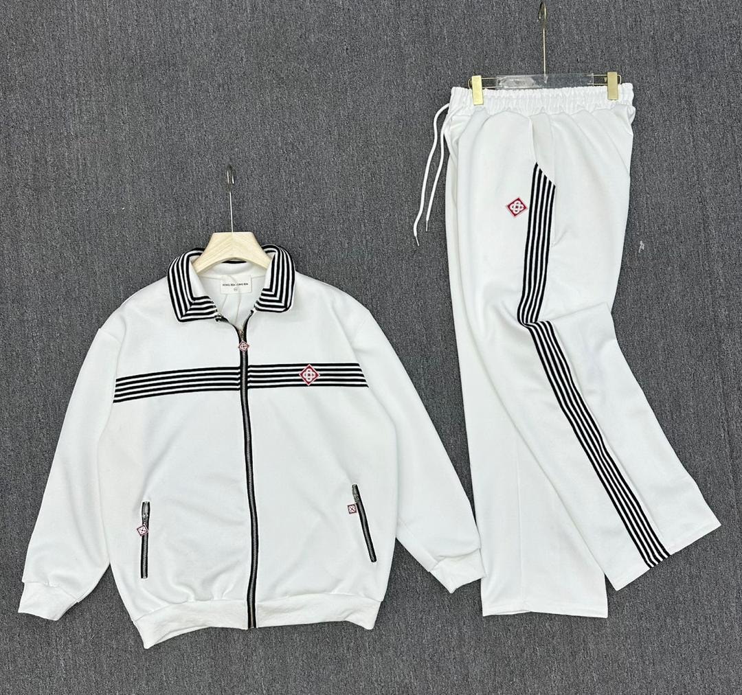 White tracksuit set laid flat showing zip jacket with striped collar and pants with side stripes.