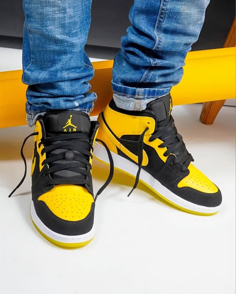 Person wearing black and yellow Air Jordan 1 Mid sneakers with blue jeans.
