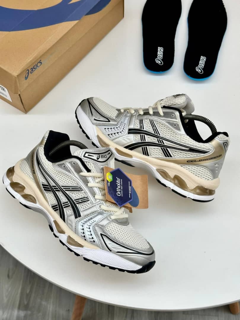 White gold and black Asics Gel-Kayano sneakers with black insoles and Ortholite tag.