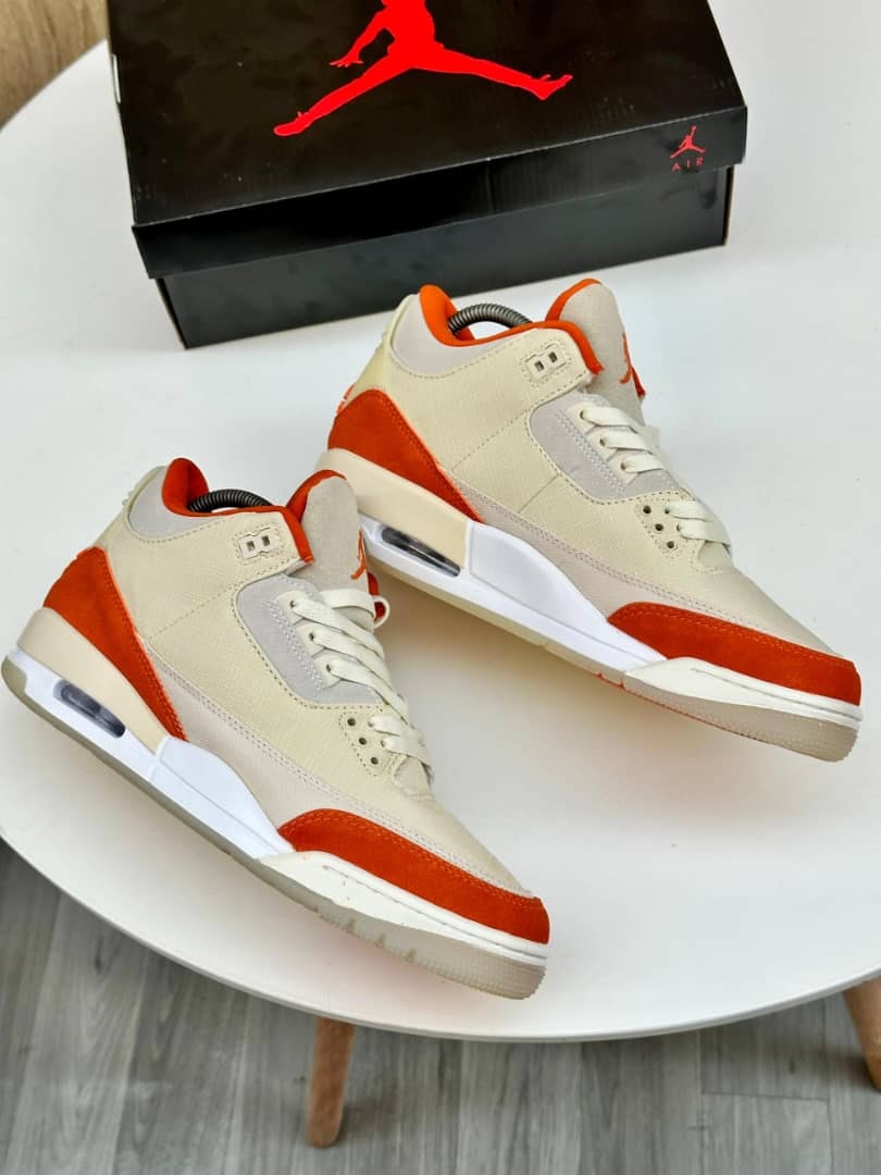 Beige orange and white Air Jordan 3 sneakers with black box in background.