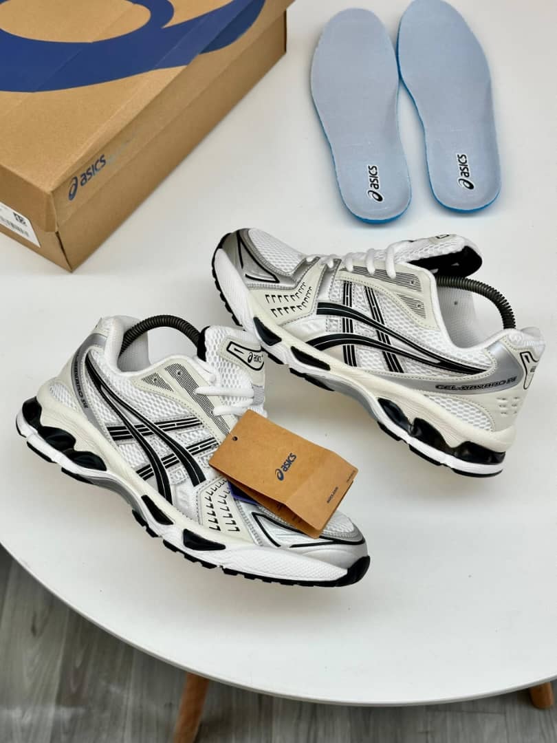 White silver and black Asics Gel-Kayano sneakers with blue insoles and box on white table.