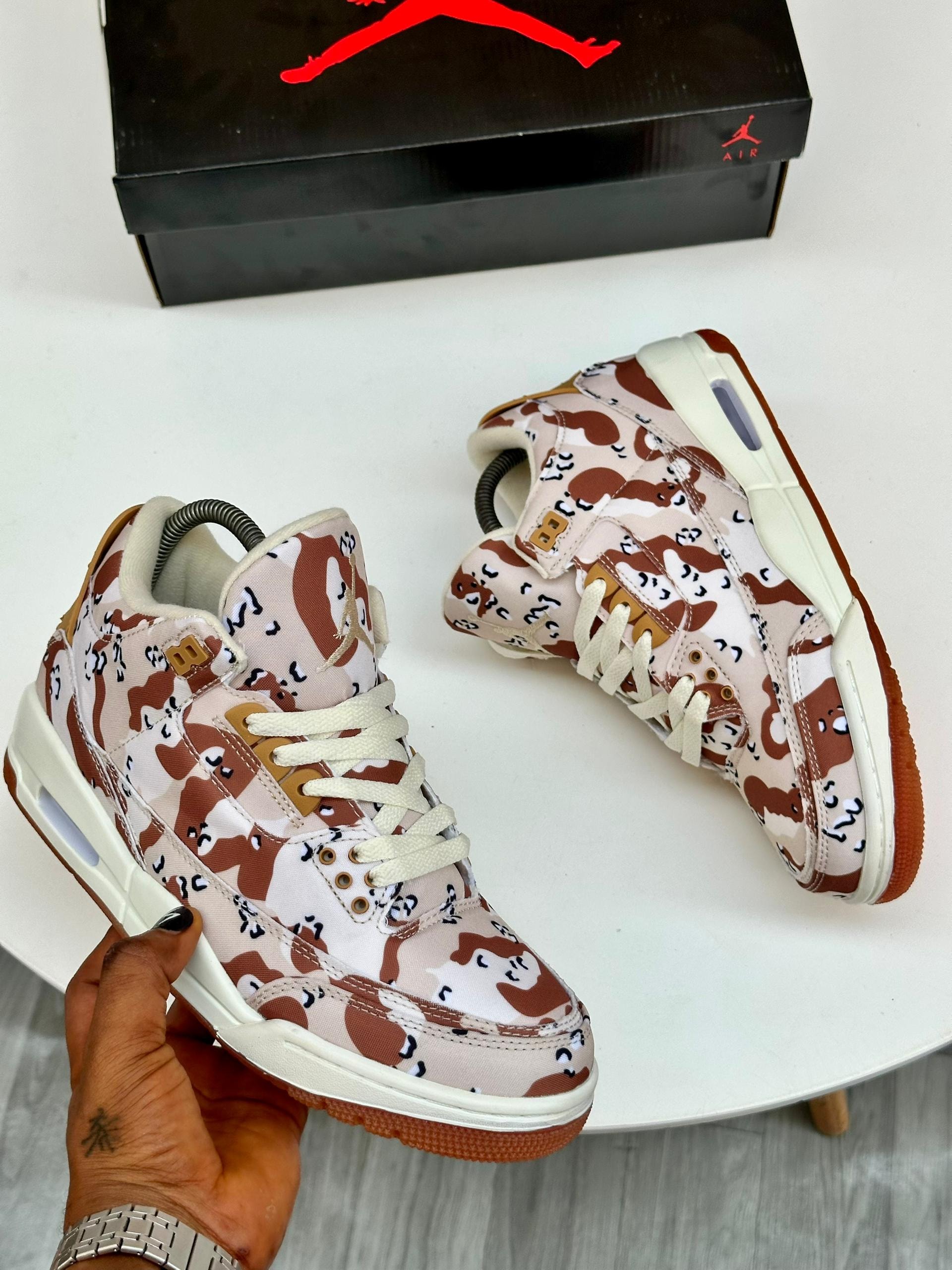 Camouflage print Air Jordan high top sneakers in brown and beige held in hand with box.
