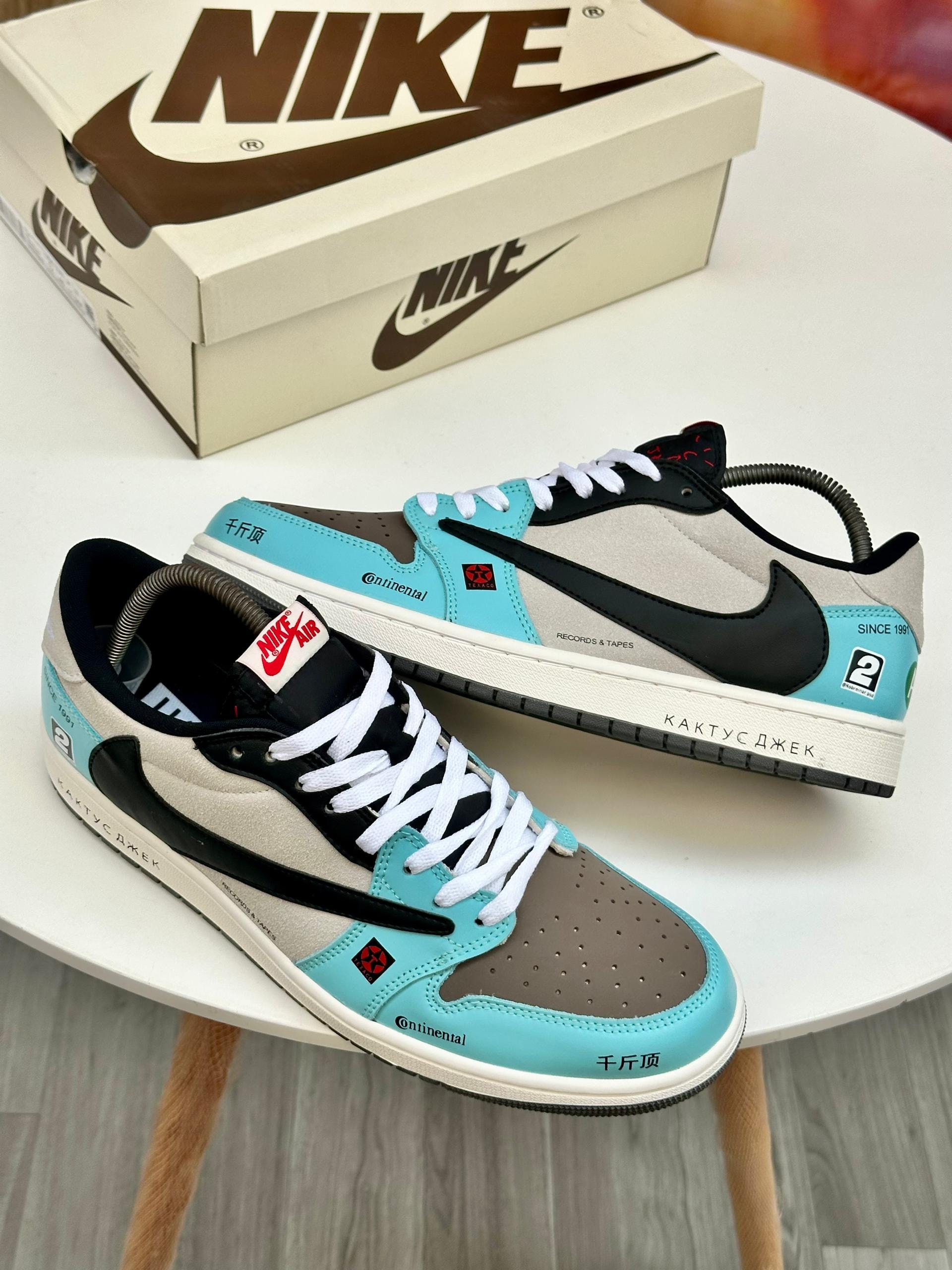 Nike Travis Scott Jordan 1 Low sneakers in turquoise black and gray with branded box in background.