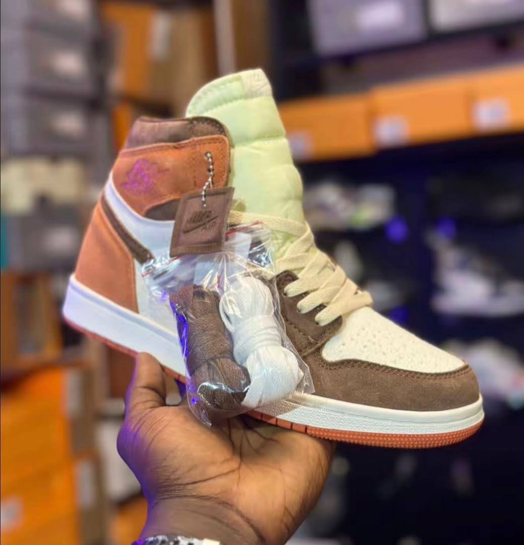 Multi-colored Nike Air Jordan 1 High sneaker in hand showing brown suede, orange, white and lime green sections with accessories.