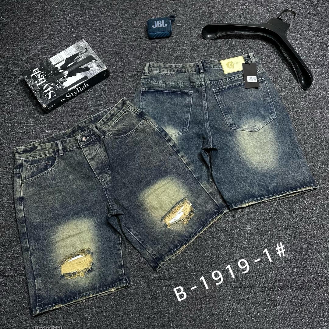 Distressed blue denim shorts with prominent knee rips and back view on dark surface.