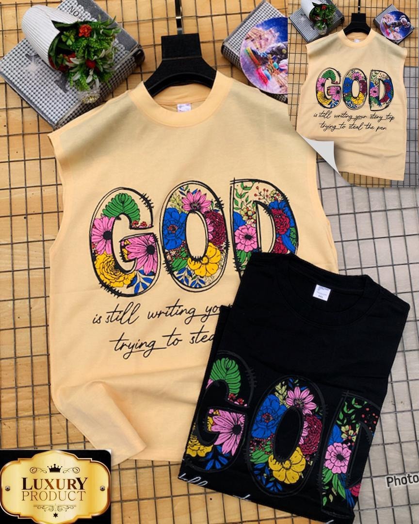 Beige and black armless tees with colorful floral GOD graphic and quote on tiled surface.
