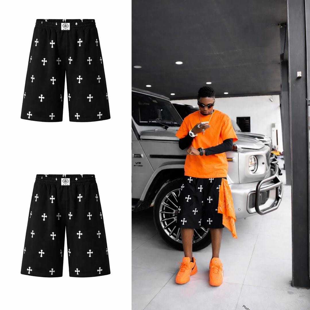 Black cross print shorts worn by model in orange outfit beside SUV, with flat lays.