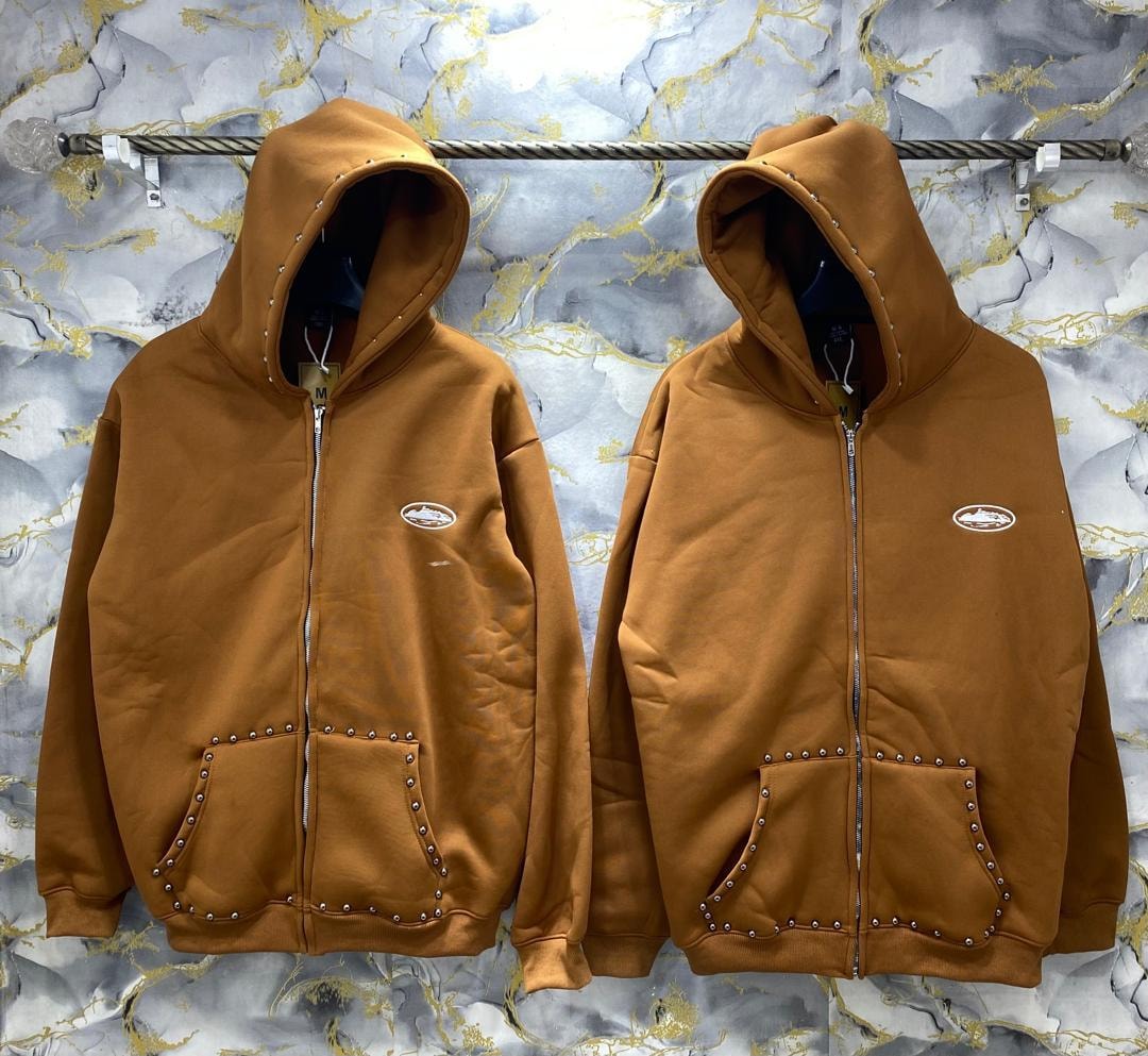 Two brown zip-up studded hoodies with metal details on pockets and hood, hanging side by side.