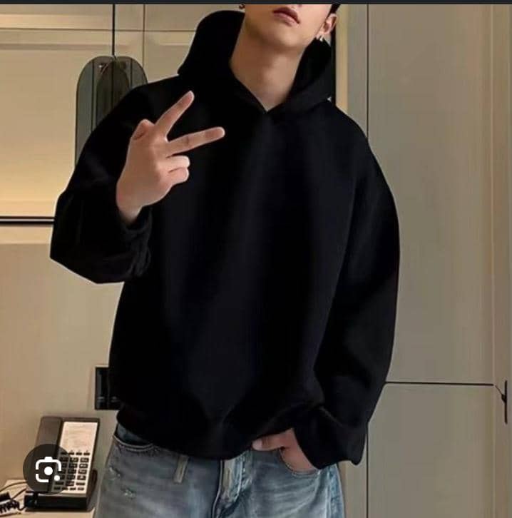 Person in black oversized hoodie posing with peace sign, hand in jeans pocket.
