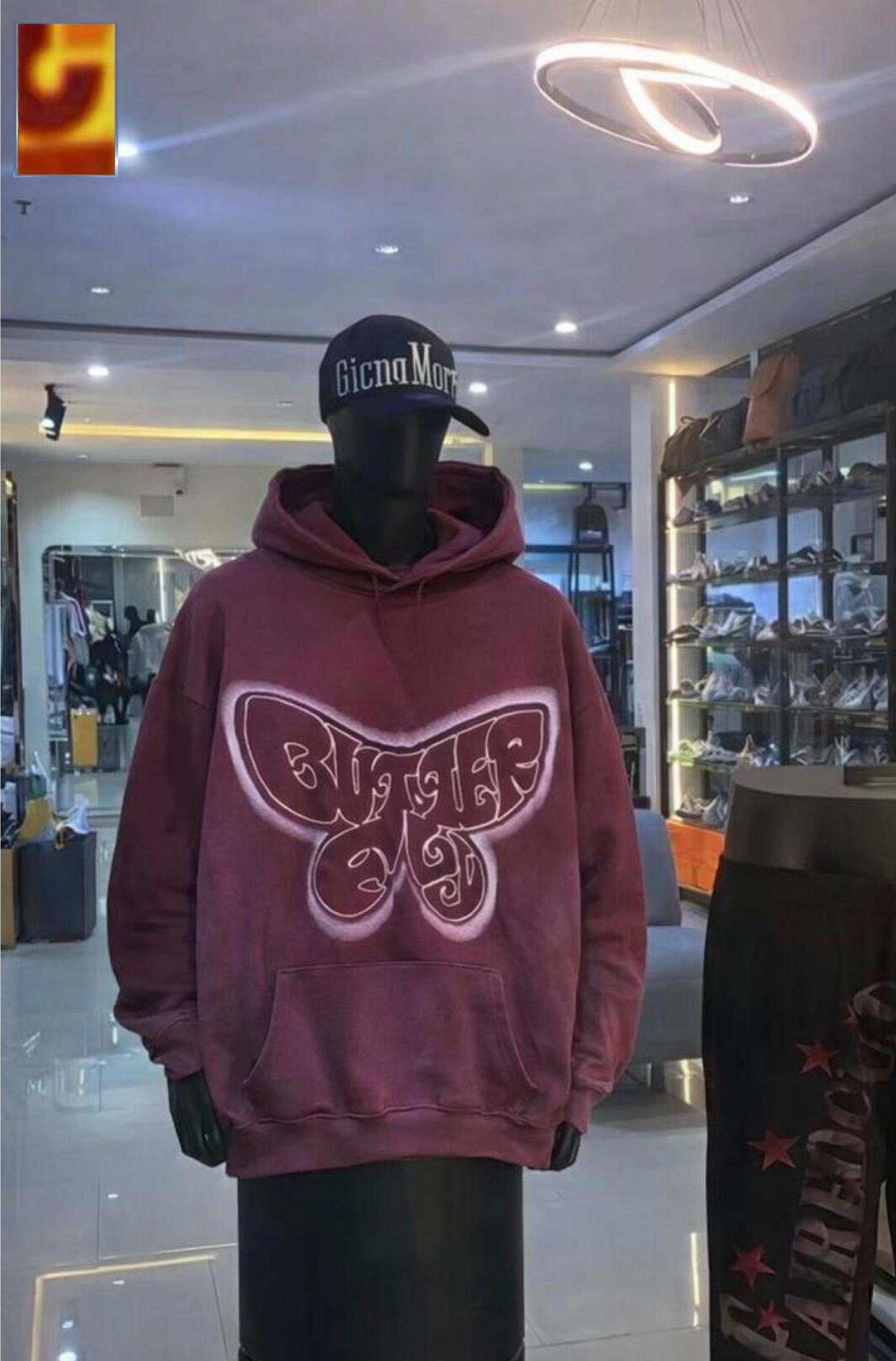 Maroon hoodie with large white-outlined butterfly graphic on mannequin wearing cap.