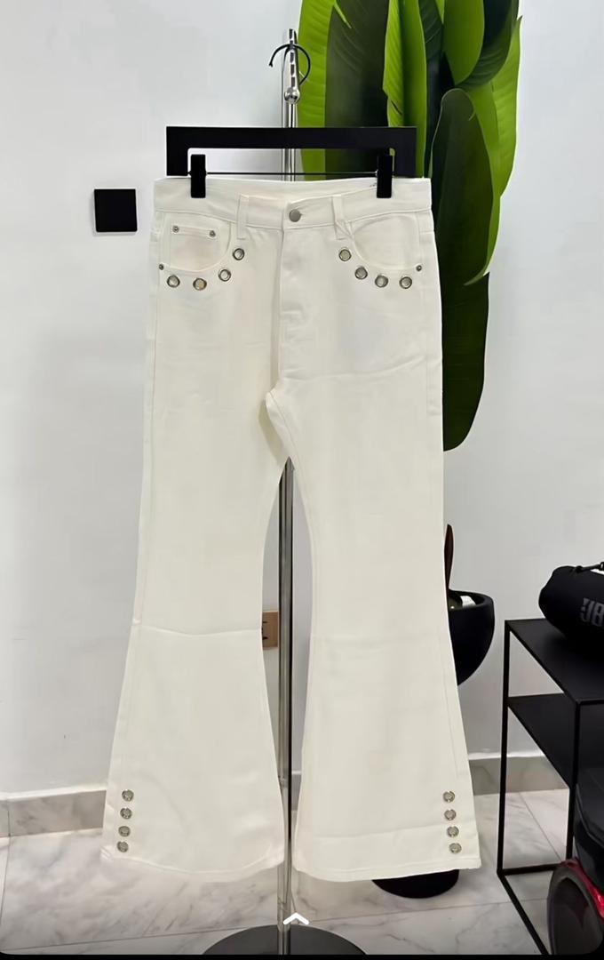 White flared jeans with silver eyelets on back pockets and hems, hanging on a display stand.