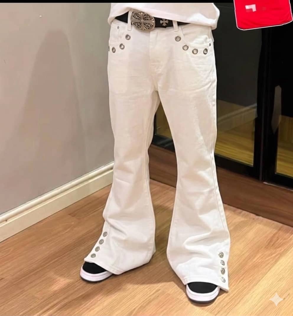 Model wearing white flared jeans with silver grommets on pockets and legs, styled with belt and slides.