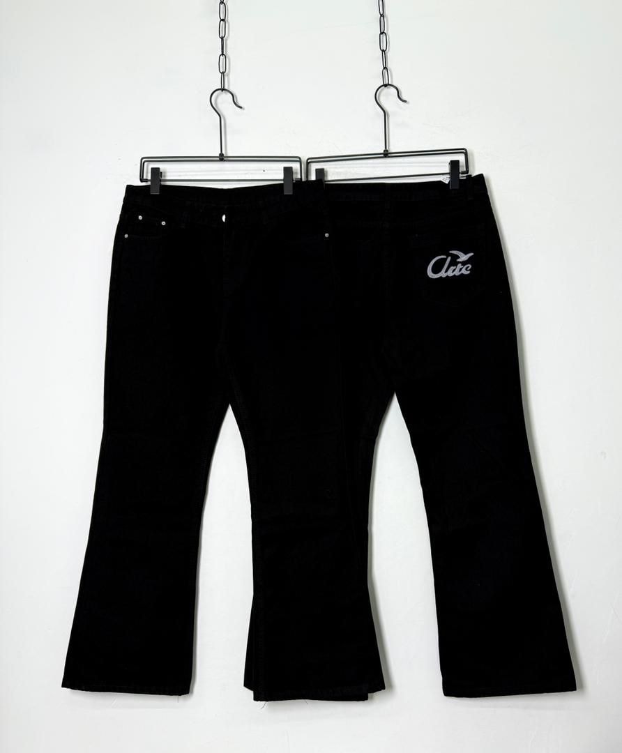 Black flared jeans hanging with white Ace embroidery visible on the back pocket.