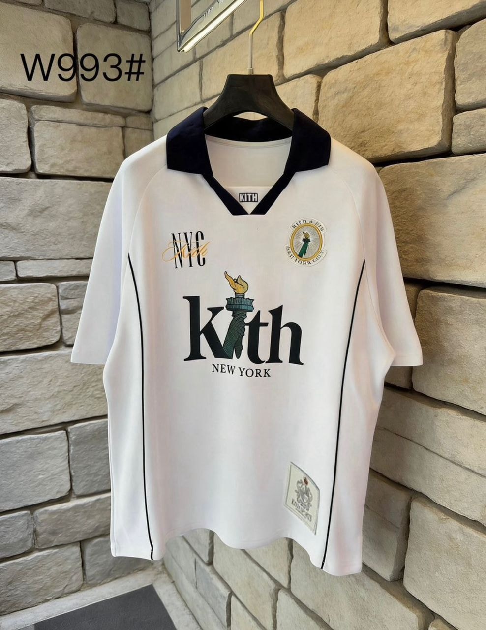 White Kith graphic V-neck tee with black collar and piping.