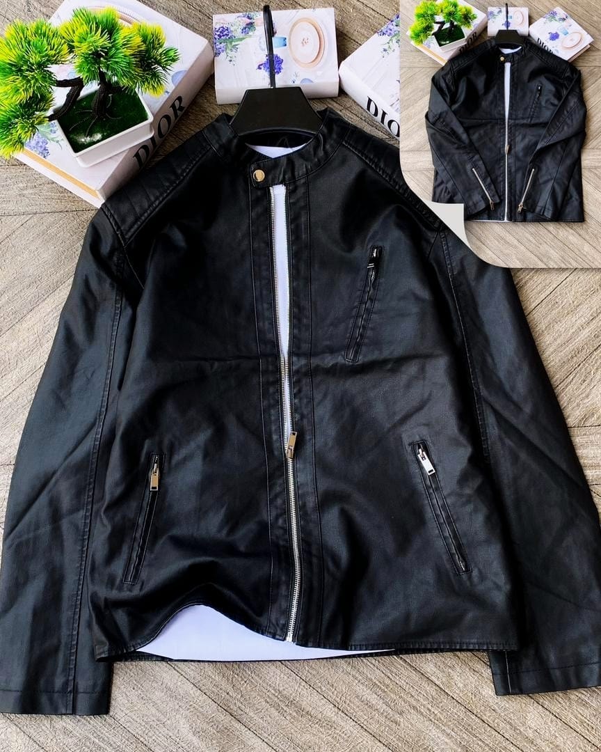 Black leather zip-up jacket laid flat on wooden surface with decorative boxes and plant.