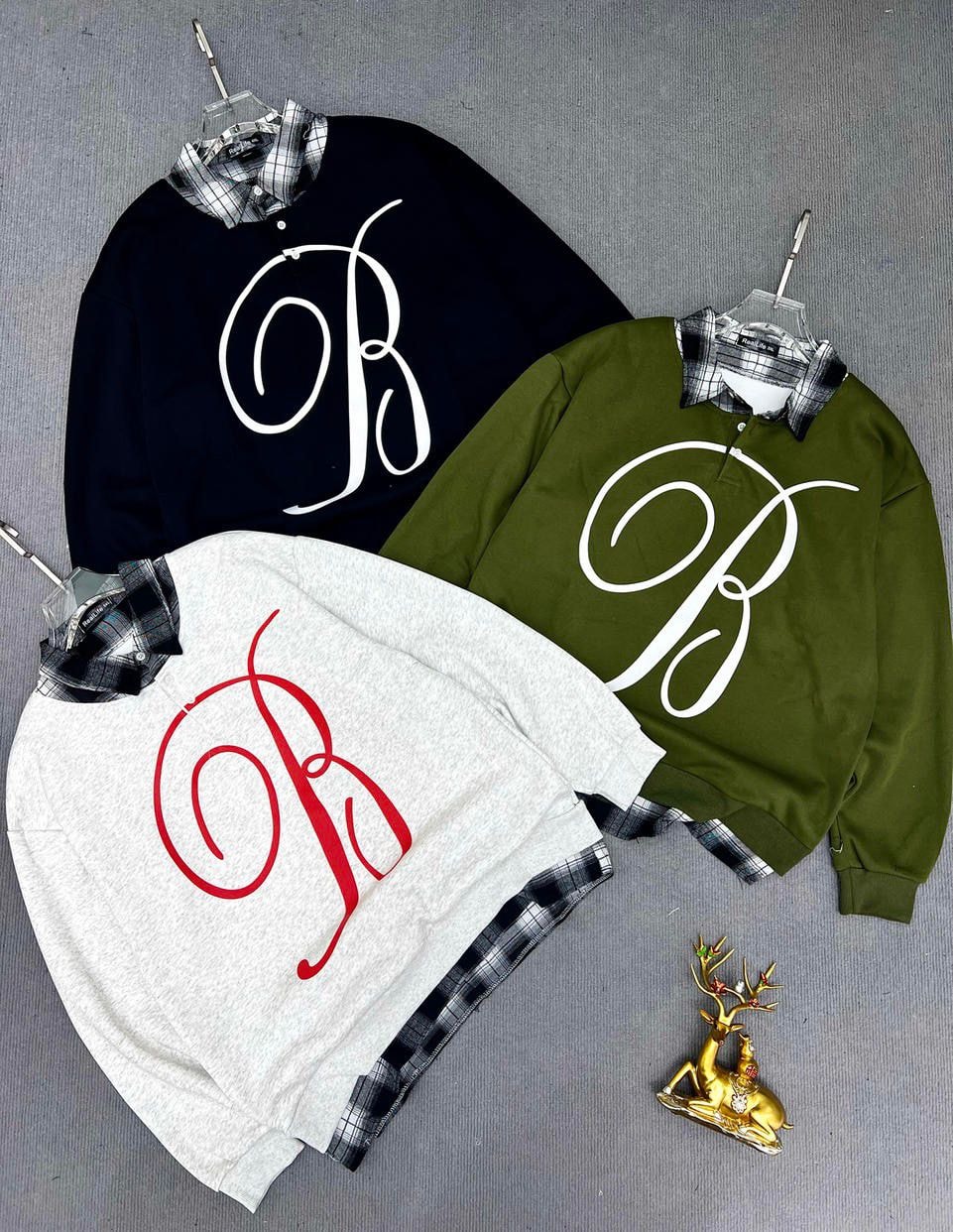 Black, olive, and gray sweatshirts with large white or red script monogram, styled over plaid shirts.