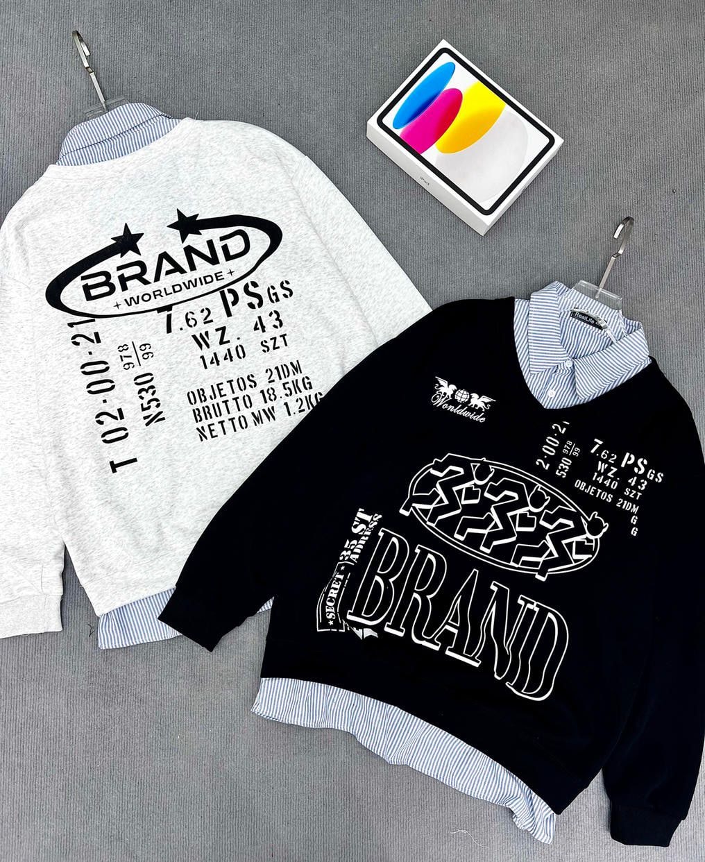Gray and black sweatshirts with BRAND graphics and text prints, layered over striped shirts on gray background.