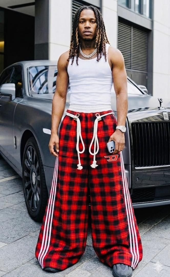 Man wearing red plaid wide-leg joggers with white tank top standing outdoors.