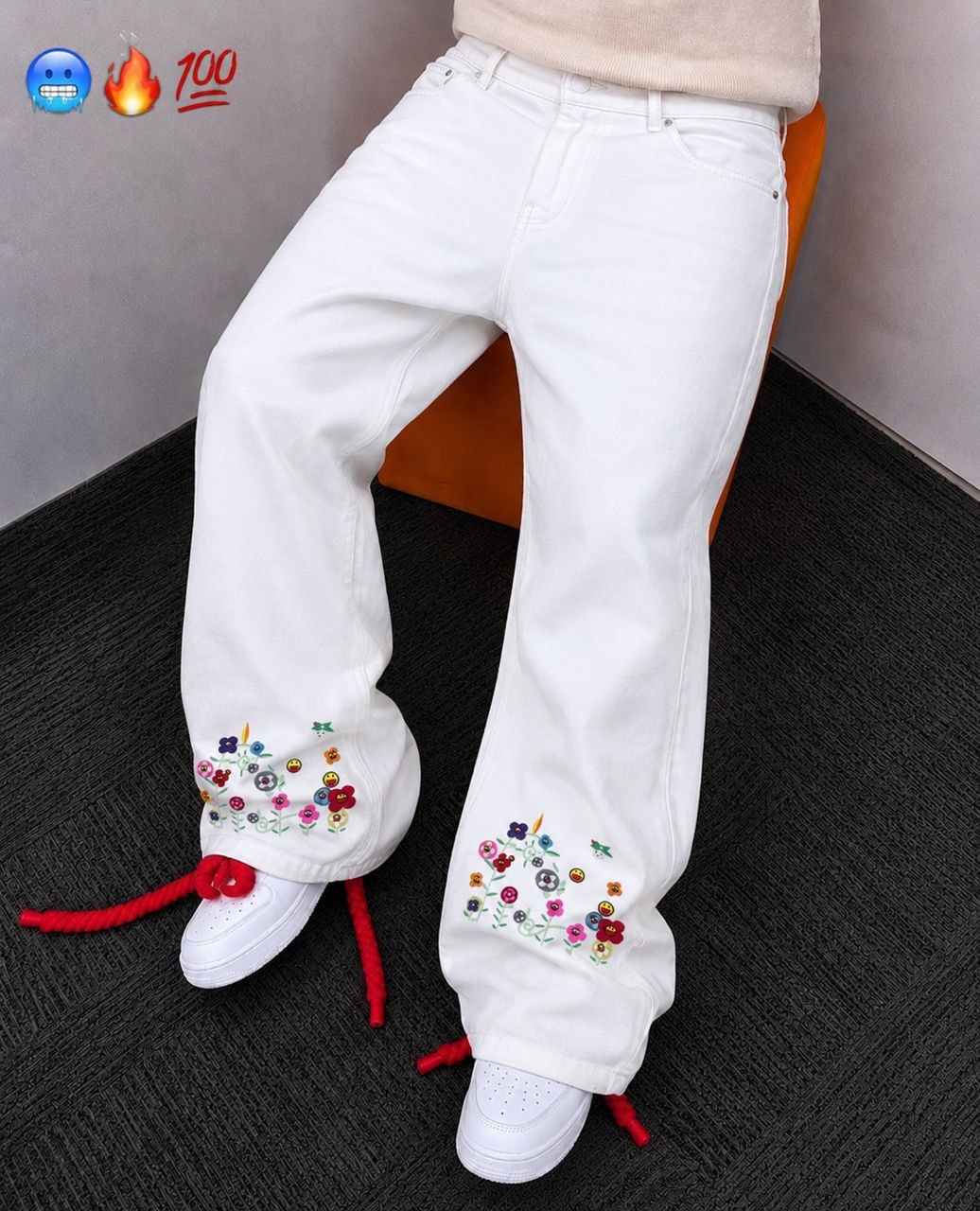 Model wearing white baggy jeans with colorful floral and smiley embroidery on the lower legs.