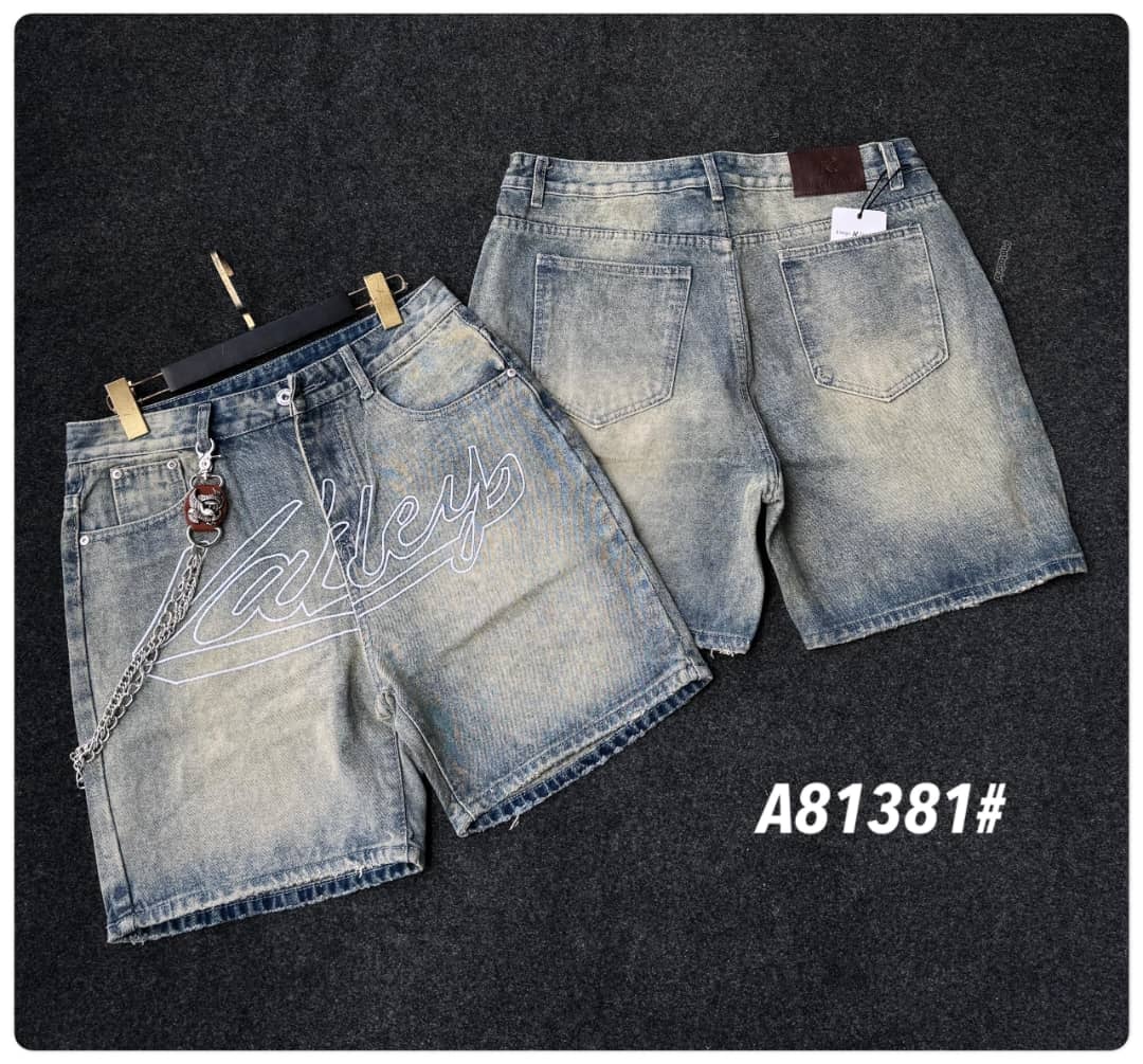 Light blue denim shorts with white script embroidery on front, chain accessory, and back view on dark surface.