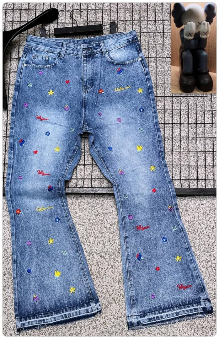 Light blue baggy jeans covered in multi-color embroidery of flowers, hearts and text, displayed flat with figurine inset.