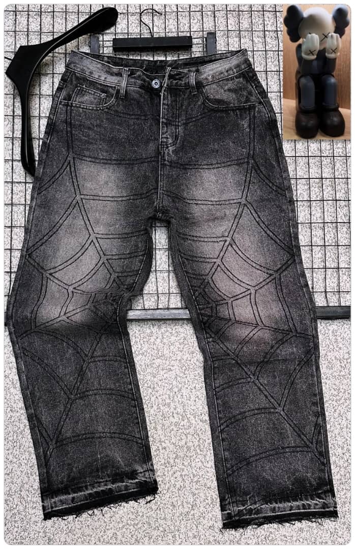 Black baggy jeans with white spider web pattern all over, displayed flat with accessories and figurine inset.