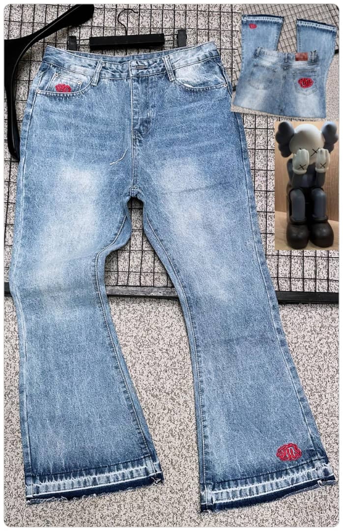 Light blue baggy jeans with red embroidery on back pocket and leg hem, shown flat on grid surface with hanger.