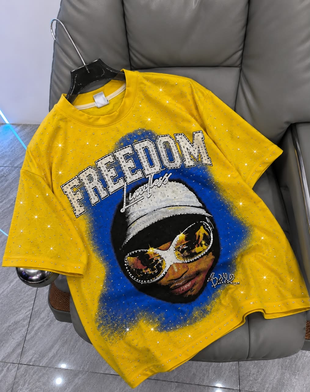 Yellow rhinestone graphic t-shirt with FREEDOM portrait design on hanger.