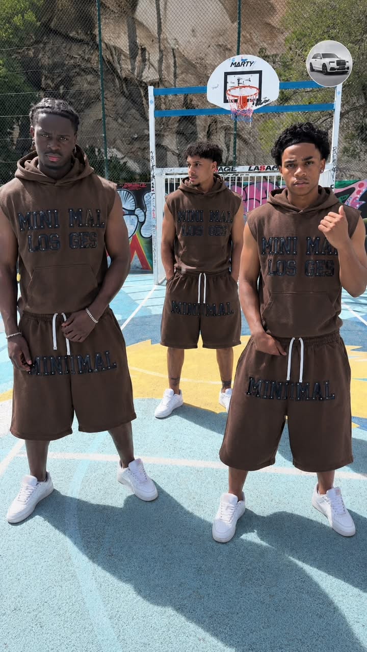 Three models wearing brown minimal sleeveless hoodie and shorts set on outdoor basketball court.