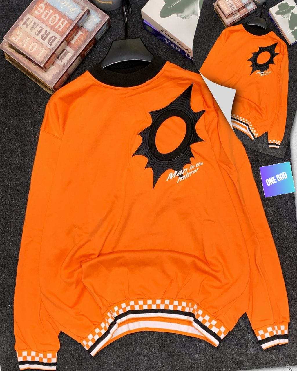 Orange Man in the Mirror sweatshirt with black embroidered logo and checkered ribbing.