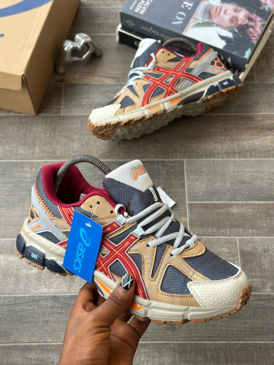 Hand holding ASICS multi-color sneaker showing side profile with blue tag.