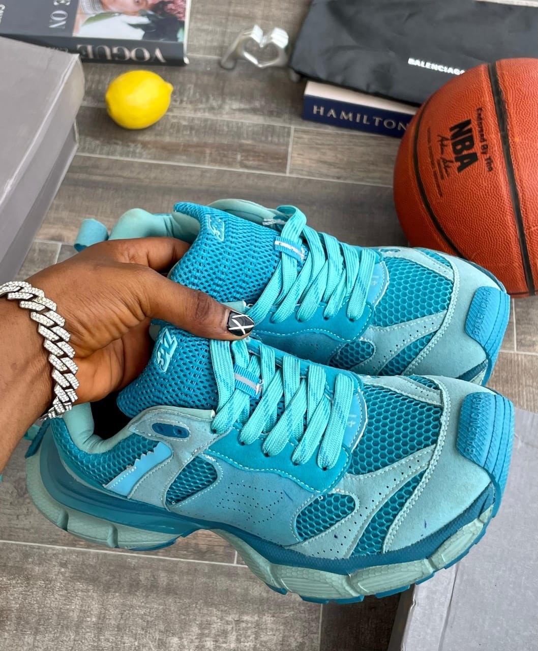 Blue New Balance sneakers held by hand with lifestyle props including basketball and books.