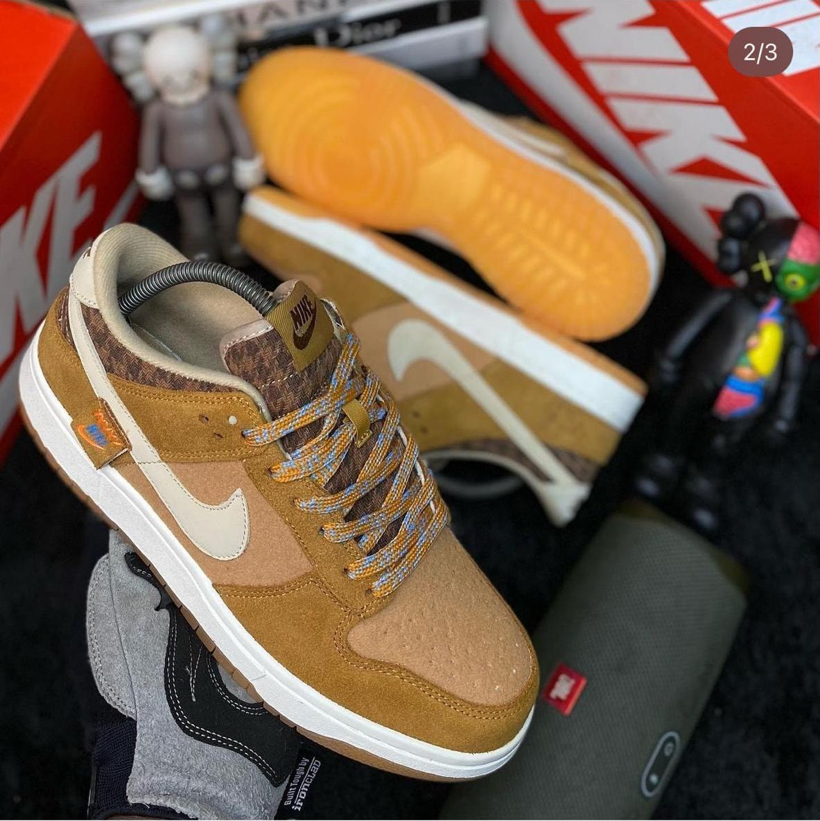 Nike Dunk Low sneaker in brown with patterned details and orange sole, shown with collectibles.