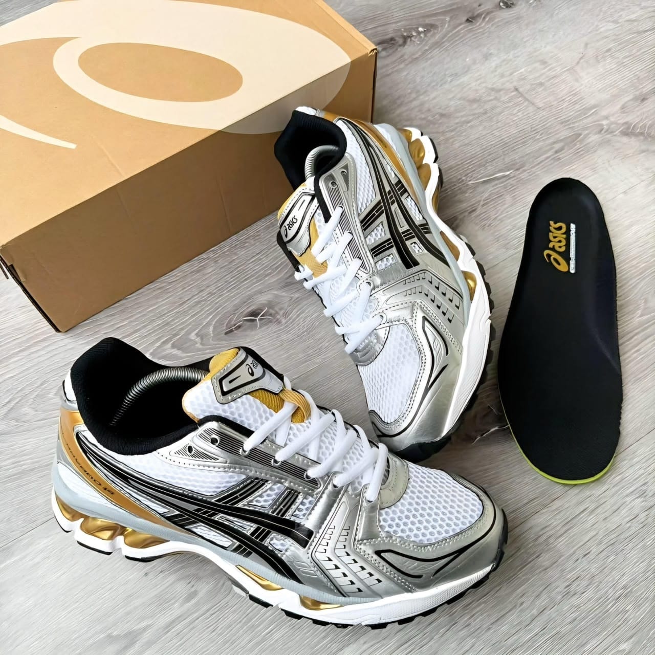Asics Gel sneakers in silver white and gold with box and insole displayed on wooden floor.