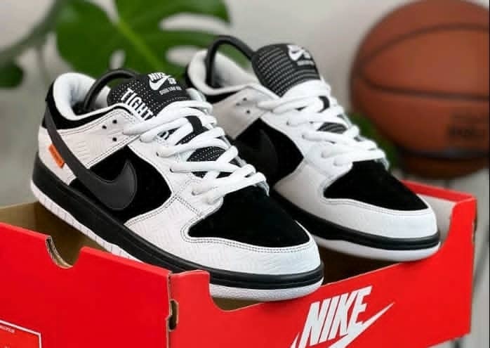 Pair of black and white Nike Dunk Low sneakers in red Nike box with basketball in background.