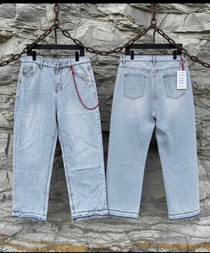 Light blue baggy jeans with frayed hems shown front and back hanging against stone wall.