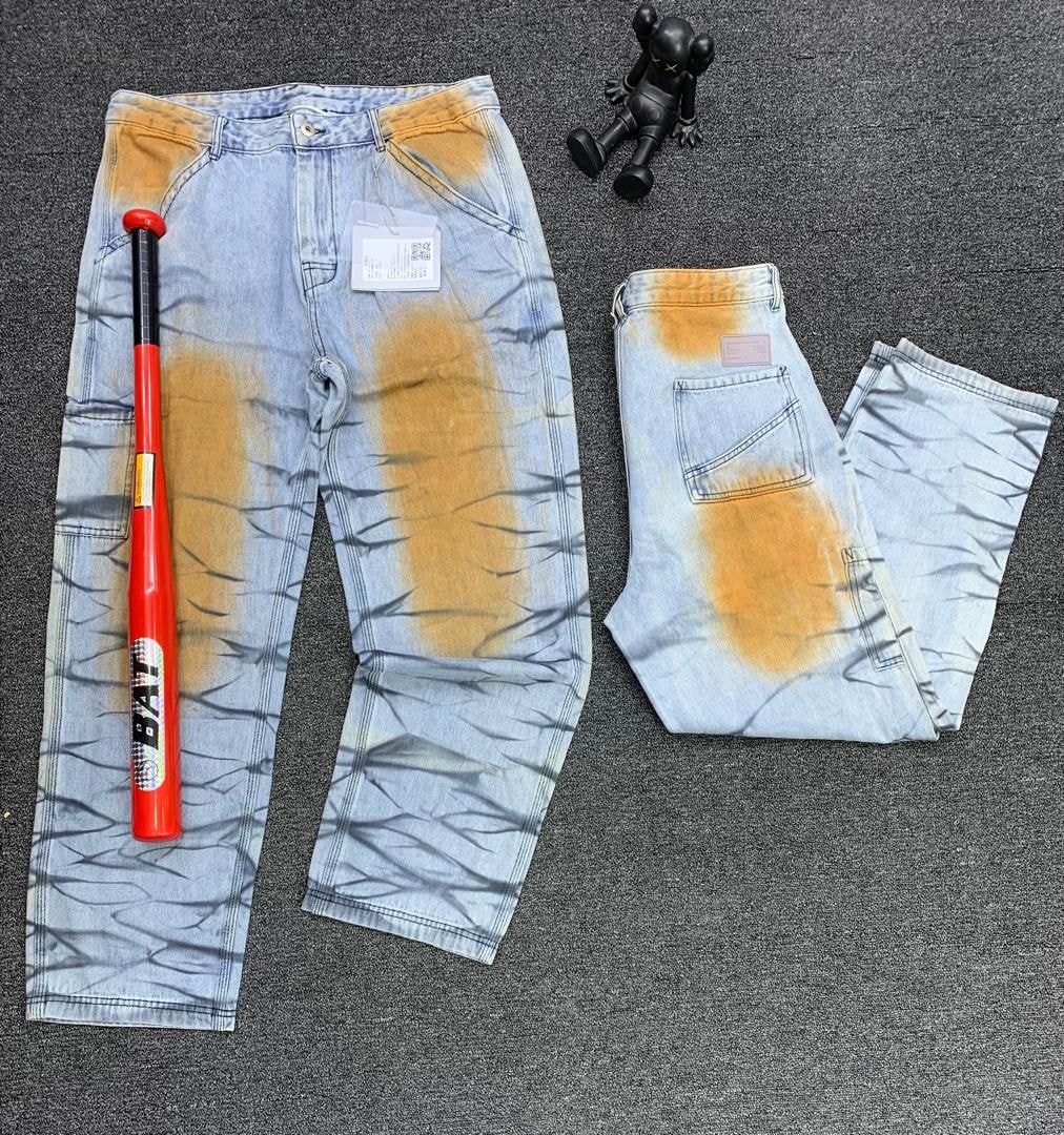 Baggy jeans with orange bleached patterns and black crackle design laid flat with baseball bat and figurine.