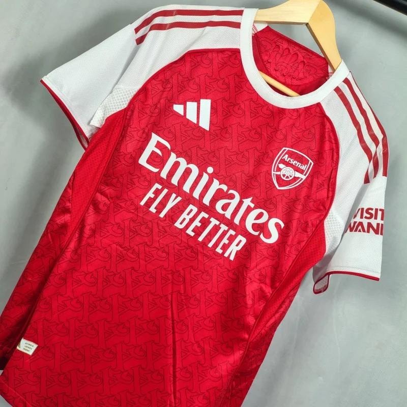 Red Adidas Arsenal jersey with all-over pattern and Emirates Fly Better text.