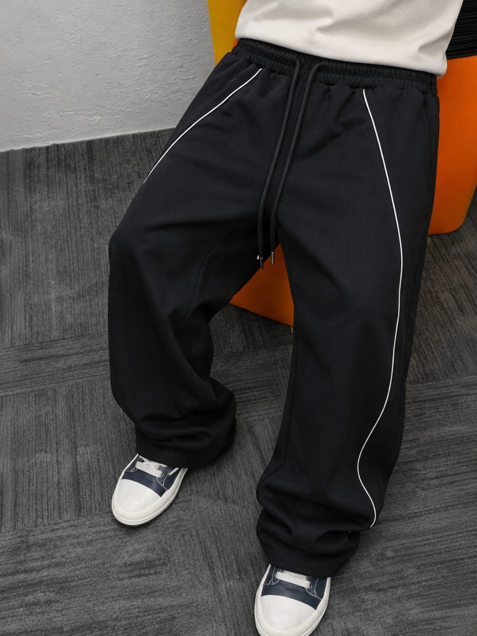Black joggers with white side piping, drawstring waist, and cuffed ankles, shown from mid-thigh down.